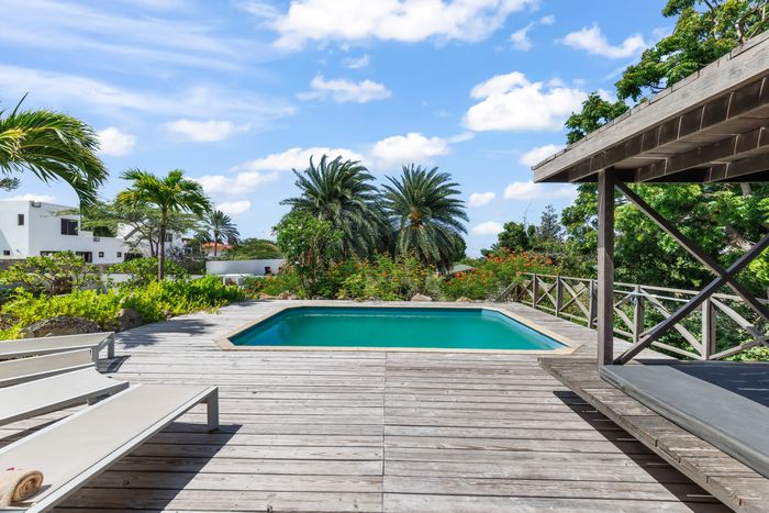 The pool with the wooden deck and the sunbeds